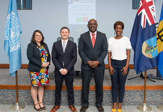 Four persons smiling for photo while standing next to the flags of United Nations, Montserrat, and Barbados