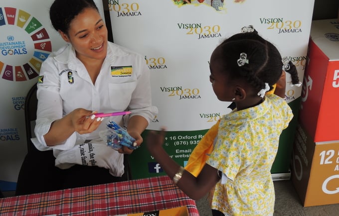 Picture showing a staff member of Vision 2030 Jamaica handing a pink pen to a little girl at the UNFPA World Population Day 2017 Commemoration Ceremony that was held in Santa Cruz, St. Elizabeth on July 11, 2017
