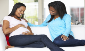 Image showing two (2) ladies sitting on a couch with one of the ladies being pregnant and rubbing tummy