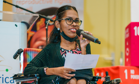 Woman in wheelchair holding microphone delivering speech