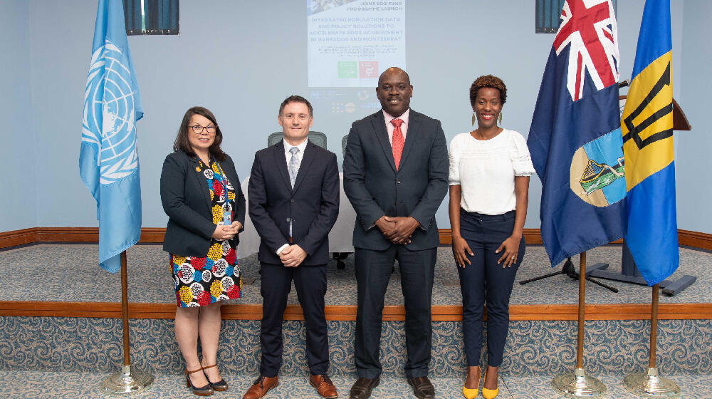 Four persons smiling for photo while standing next to the flags of United Nations, Montserrat, and Barbados